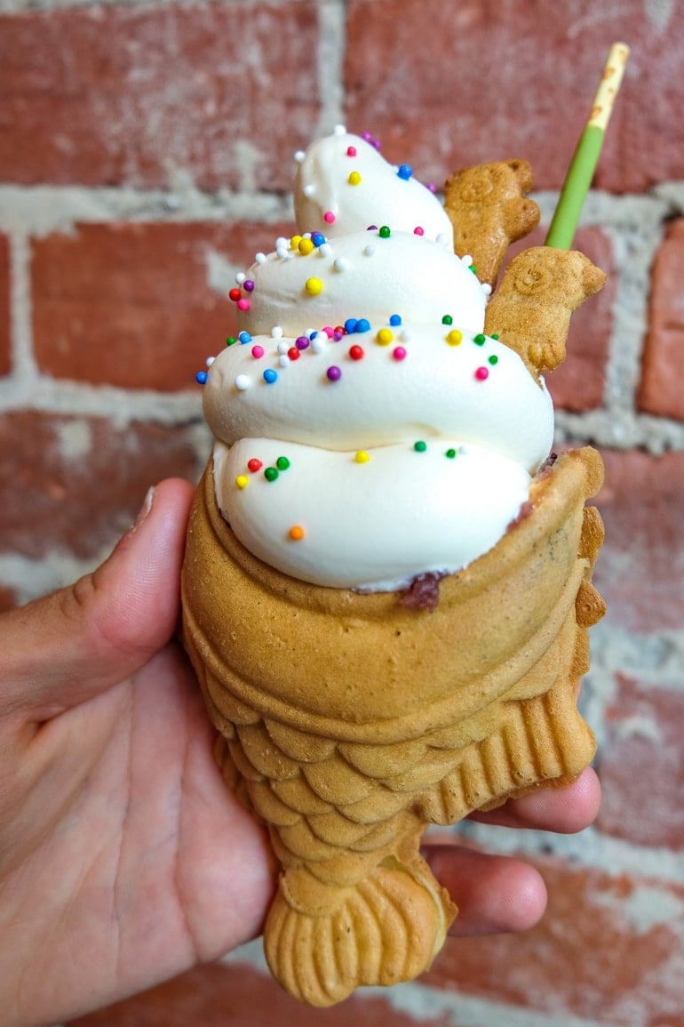 white ice cream with sprinkles in fish shaped cone with red brick behind