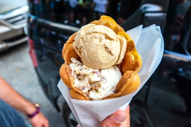 ice cream in waffle cone held in hand with car behind