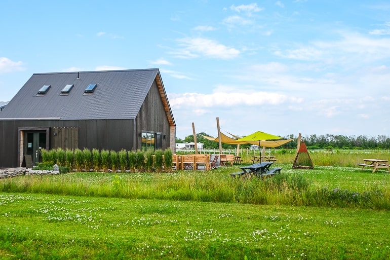 small grey barn building with small patio and green fields around 