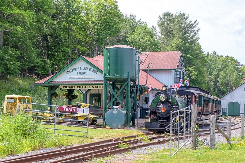 small train station with old steam train and trees behind in huntsville ontario