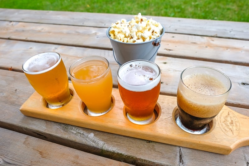 four beer tasting glasses in wooden holder on wooden table with popcorn