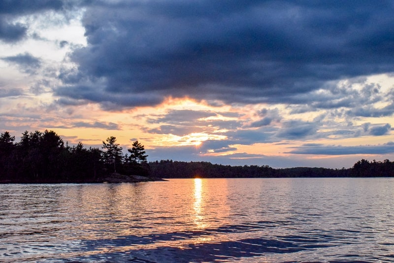 sunset with dark clouds over lake with trees in ontario