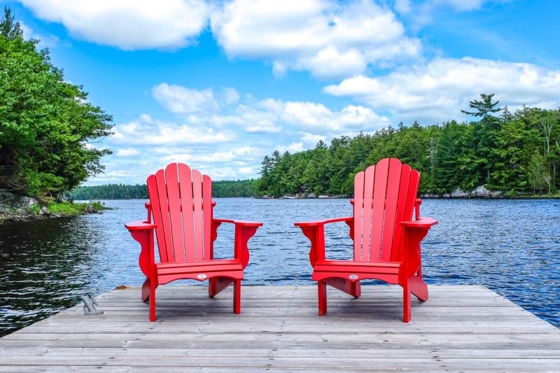 red chairs on wooden dock with lake and green trees behind