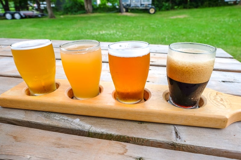 flight of four craft beer glasses in wooden holder on wooden picnic table