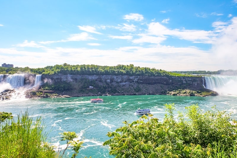 two boats on blue river with niagara falls behind