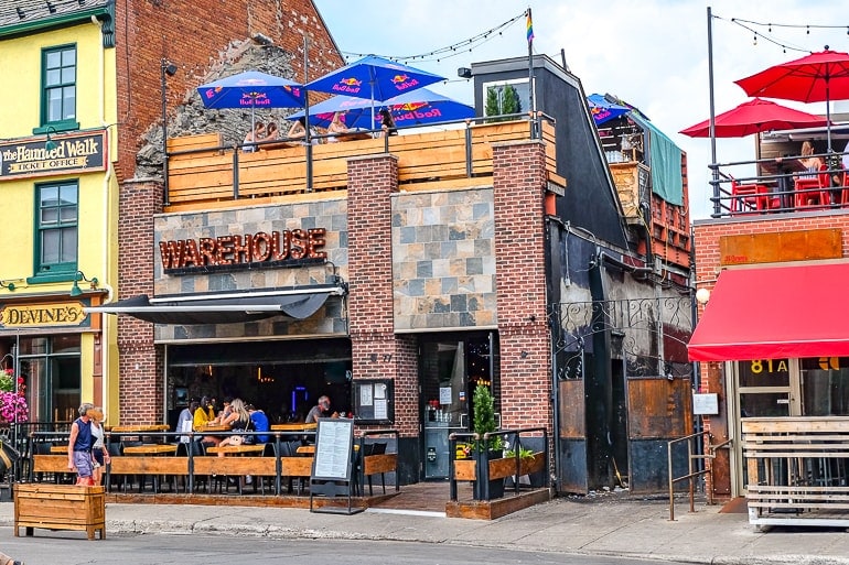bar building with wooden front patio and upper patio with blue umbrellas.