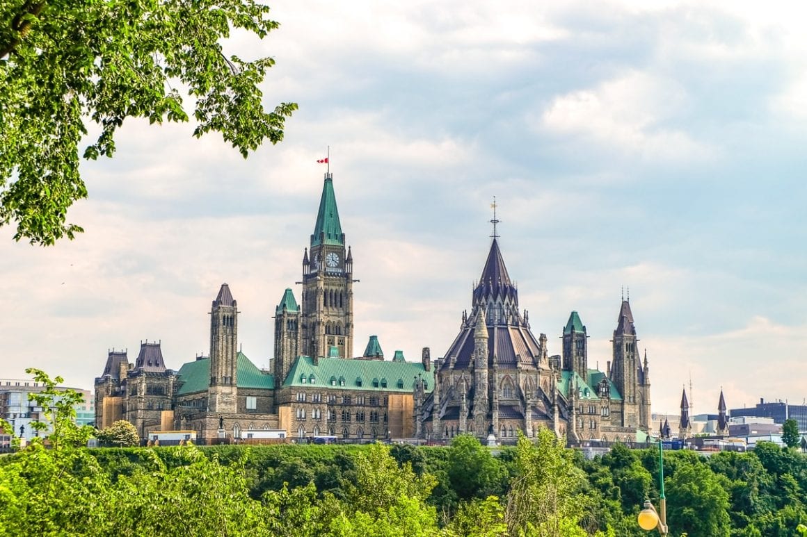 tower of canadian parliament building in distance with green trees in front