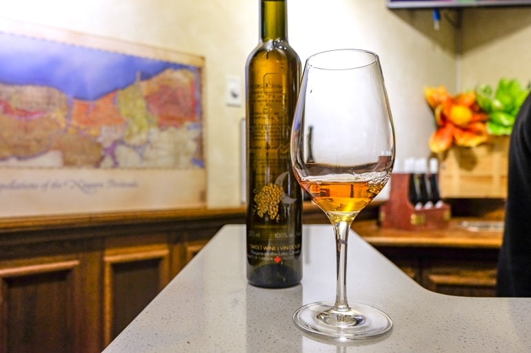 tasting glass of ice wine on counter with bottle behind.