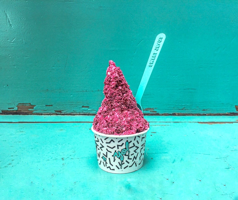 pink ice cream in cup with spoon and blue background 