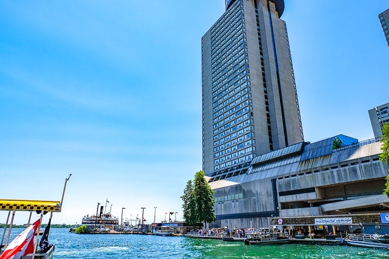 tall hotel building at toronto waterfront with boats in water beside and blue sky behind.