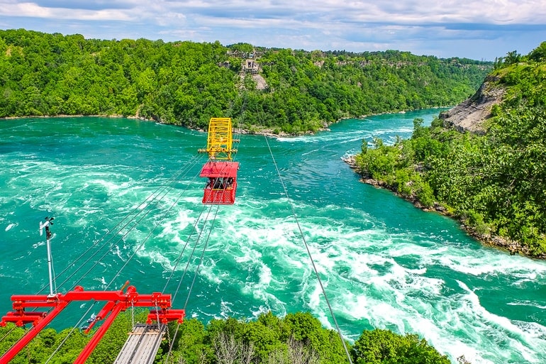 red cable car hanging over white water in niagara river