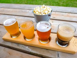 flight of four craft beer on wooden picnic table with popcorn behind