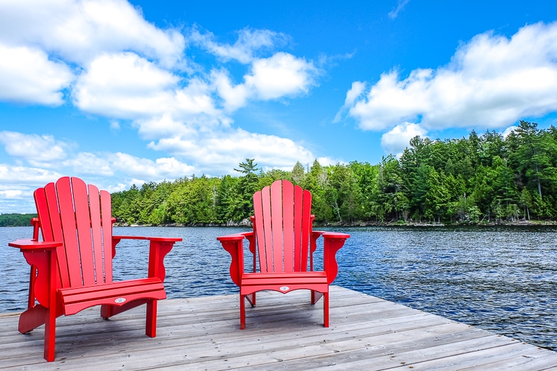 red chairs on wooden dock with lake and trees behind