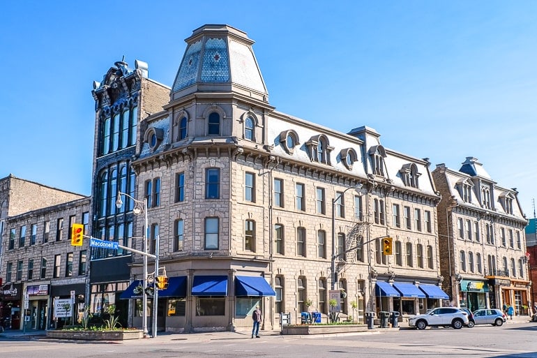 old stone building at downtown intersection with cars on street and blue sky
