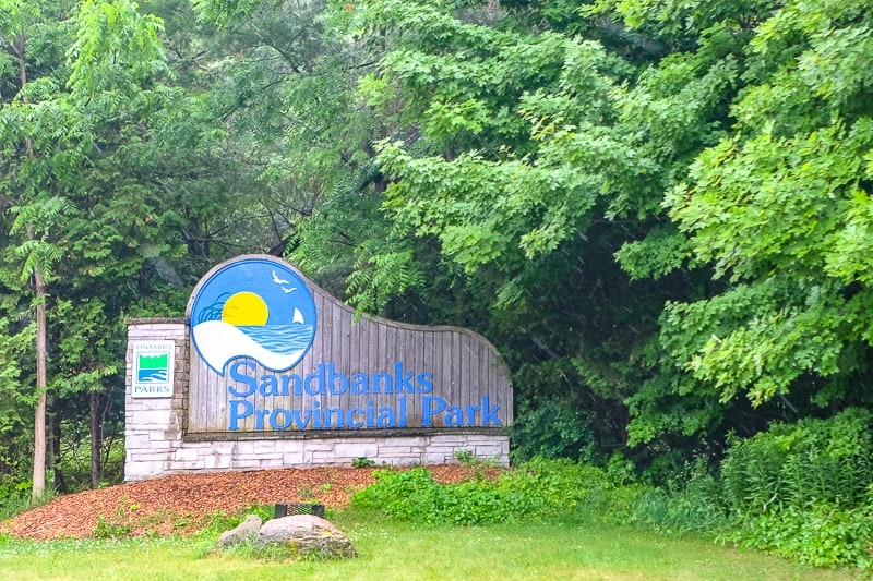 wooden entrance sign to sandbanks provincial park with green trees behind