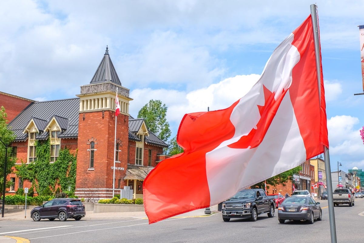 canada flag by small town building with cars behind.