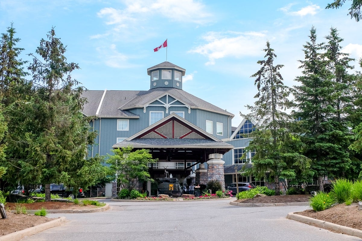 blue muskoka resort entrance with green trees and parking lot in front