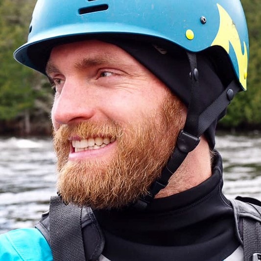 smiling man with river helmet on with river flowing behind.