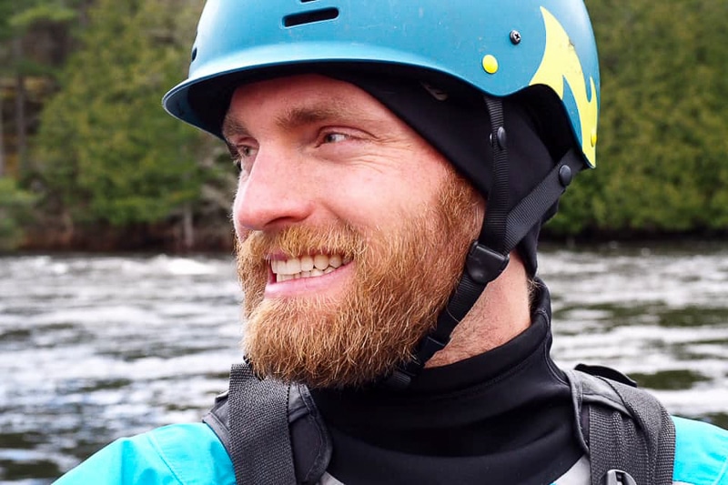 smiling man with helmet and life jacket on with river behind