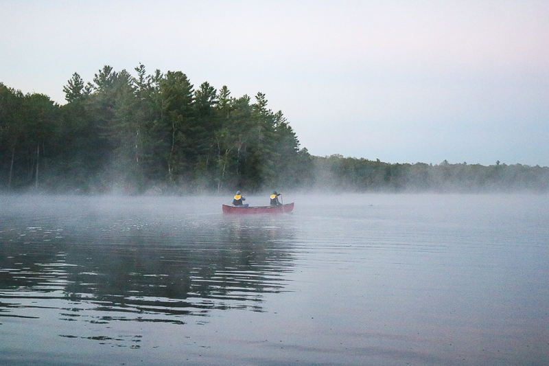 red canoe with two paddlers crossing misty lake