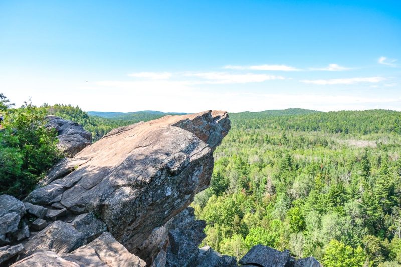 large rock extending off cliff over top of green trees in below valley