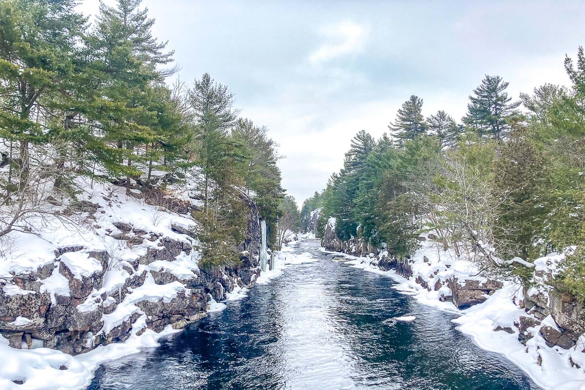 blue river cutting through snowy rock cliffs with trees above in ontario