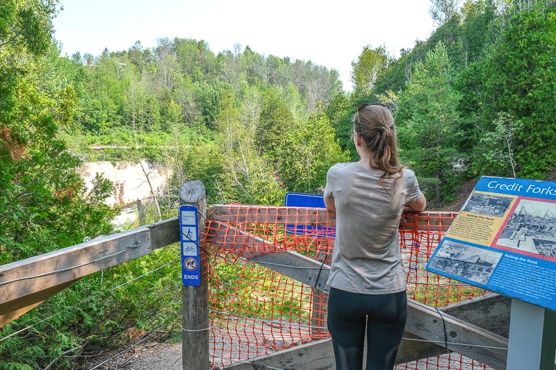 woman standing behind orange fence on trail with cataract falls behind