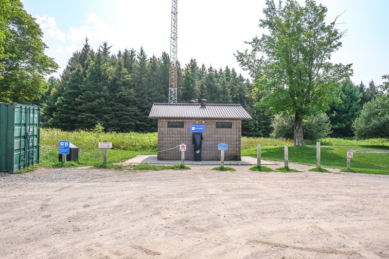 small structure with gravel parking lot in front and trees behind