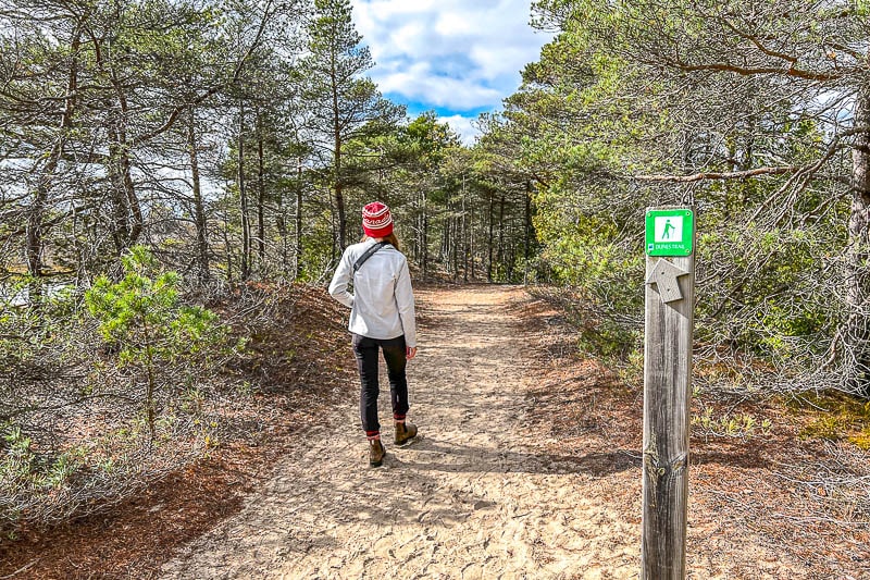 girl in red toque walking on sandy trail with wooden tail marker beside.