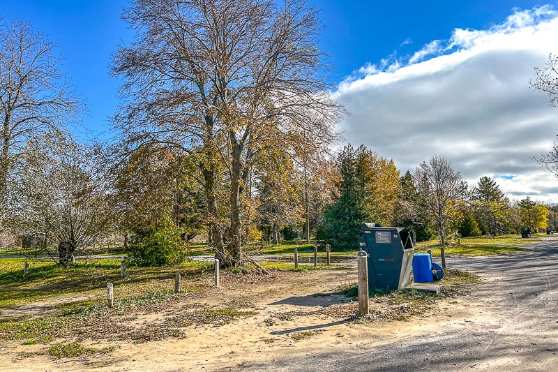 garbage dumpster in sandy parking lots with trees behind