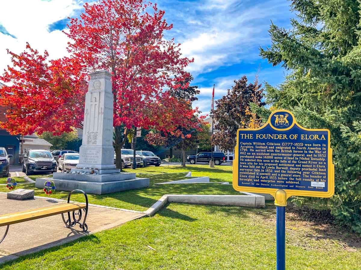 historic sign with stone cenotaph behind with colourful autumn trees around in elora ontario.