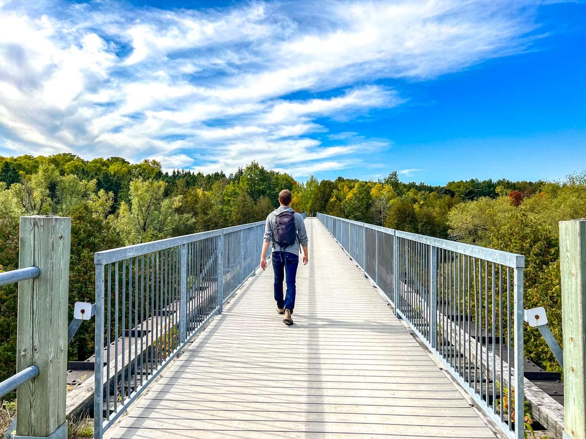man with backpack walking across large trestle bridge path with railings ob both sides.