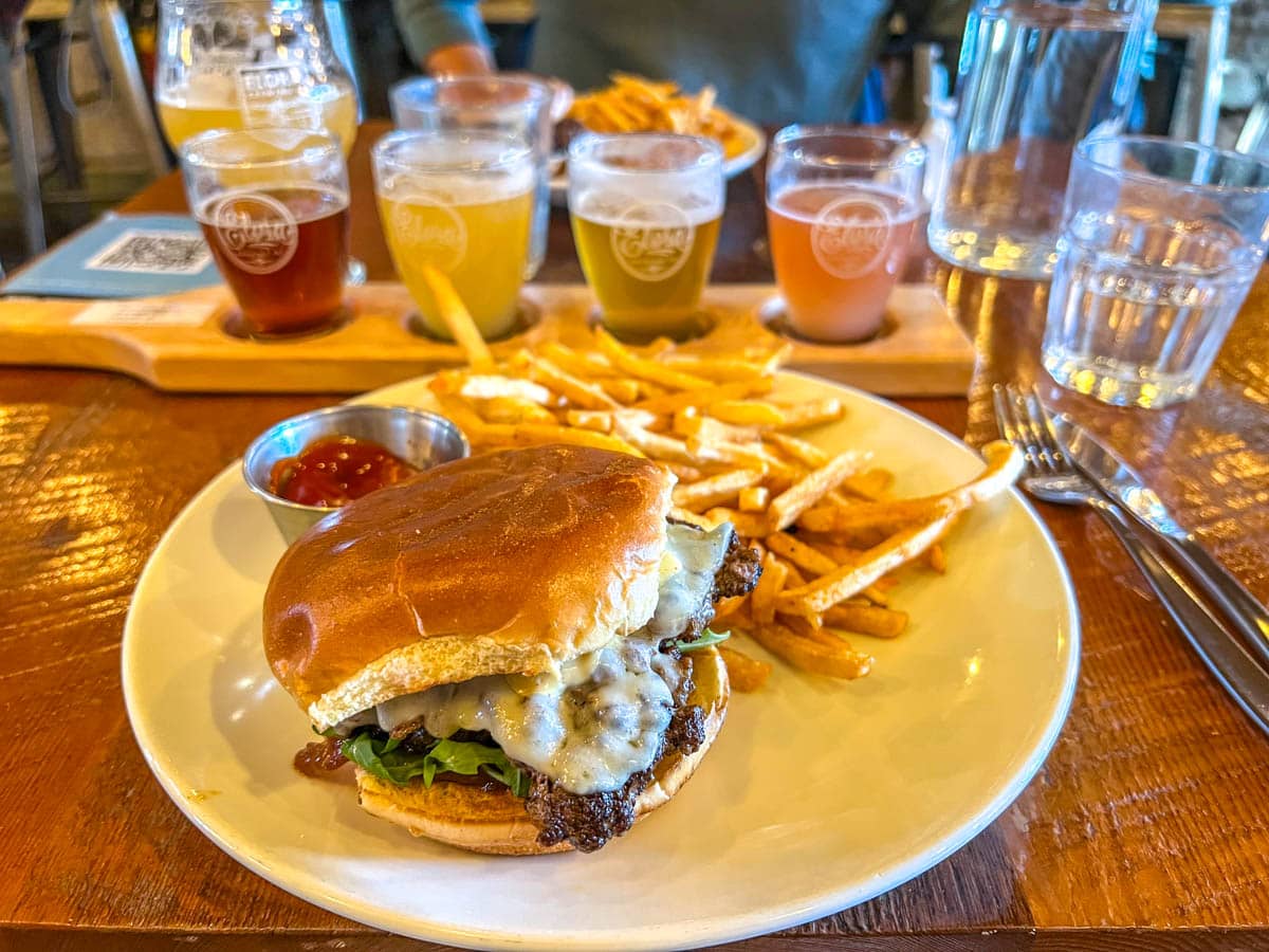 hamburger on plate with fries with sampler beers behind on table at elora brewing co.