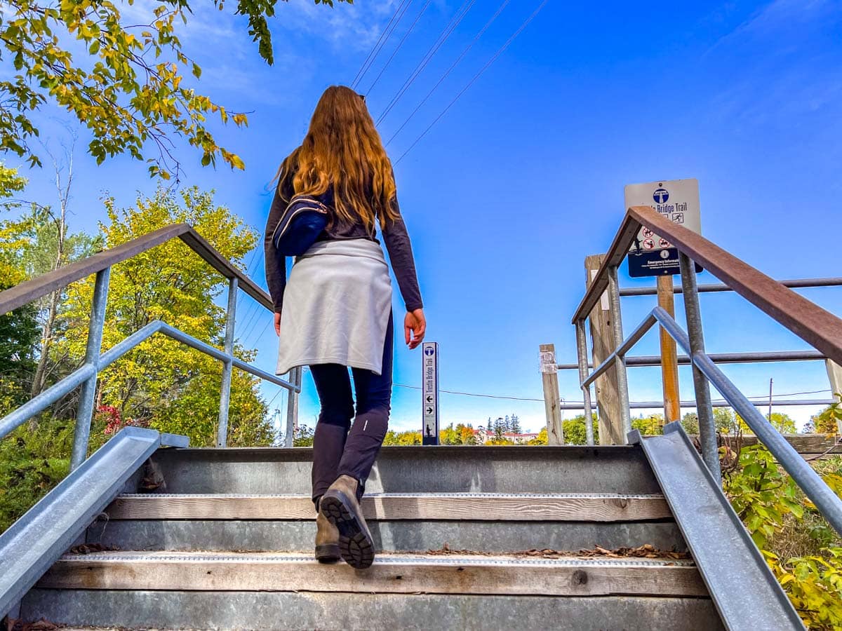 woman with sweater wrapped around waist climbing stairs to another trail.