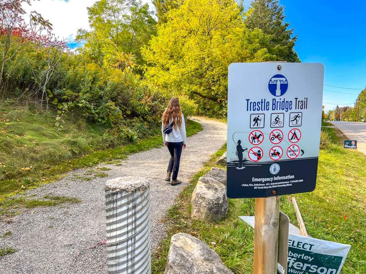 woman walking on trail with trail sign and rocks in foreground.