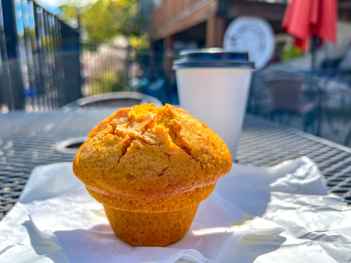orange muffin on wrapper sitting on patio table with coffee in takeaway cup behind.