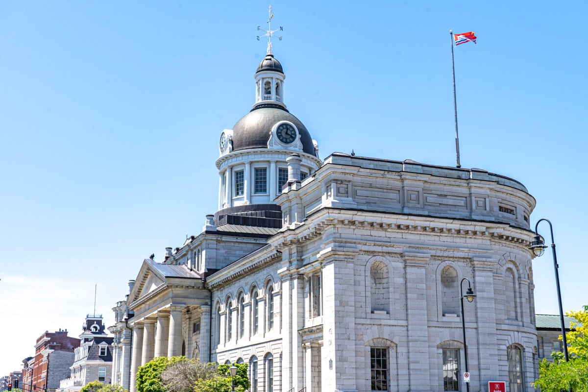 large historic city hall with clock and flag pole in kingston ontario.