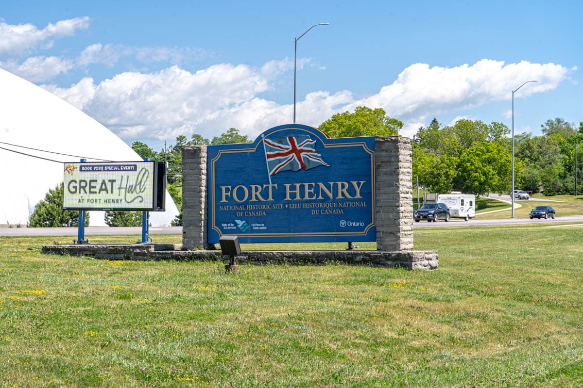 blue entrance sign in glass to fort henry with summer sky above.