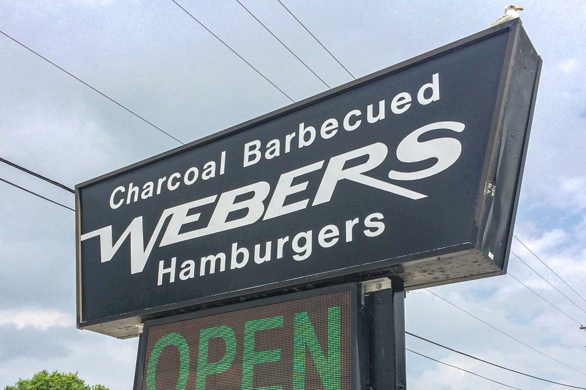 black road sign that says webers hamburgers on it with seagull on top.
