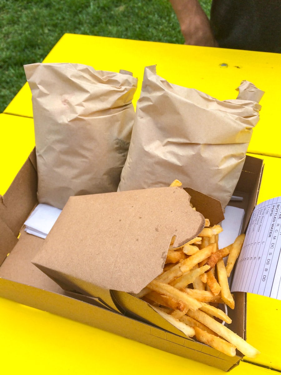 paper bags with burgers inside beside fried on a paper tray.