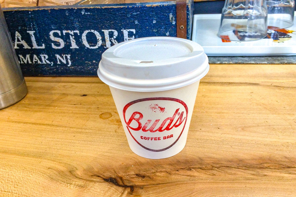white takeaway cup with red writing sitting on wooden counter.