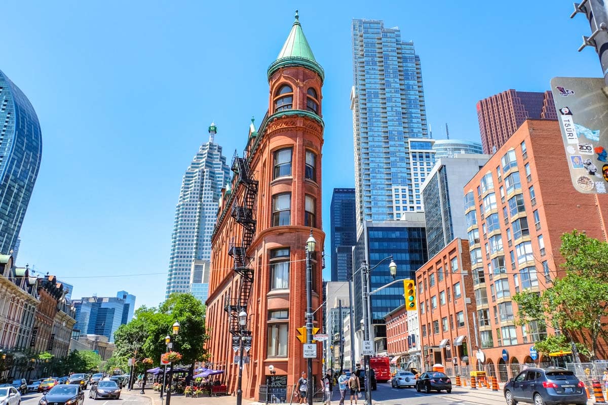 red brick flatiron building in toronto with tall buildings behind.