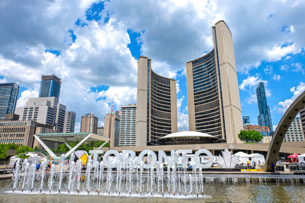 iconic curved buildings in toronto with fountain in front and toronto sign behind.
